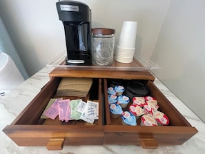 A drawer with a coffee maker, a jar, and stacks of white cups.
