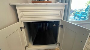 Une cuisine compacte dotée d’un réfrigérateur encastré, d’un plan de travail blanc et d’une fenêtre donnant sur un balcon.