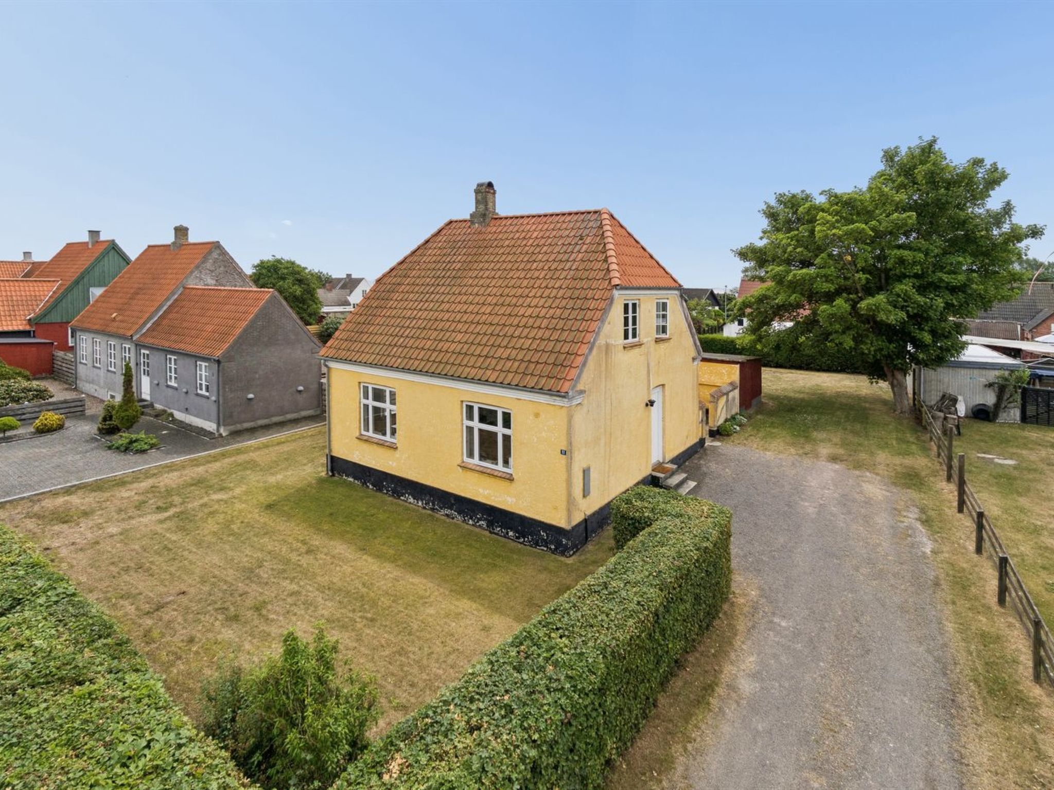 A yellow house with a red roof, surrounded by a well-maintained lawn and a gravel path.