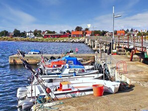 Ein Hafen mit vertäuten Booten, eine Anlegestelle, die sich ins Wasser erstreckt, und Gebäude im Hintergrund.