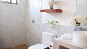 A bathroom with a shower, toilet, and sink. There are wooden shelves with flowers and a hanging plant.