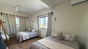 A bedroom with two beds, a ceiling fan, an air conditioning unit, and a window with curtains.