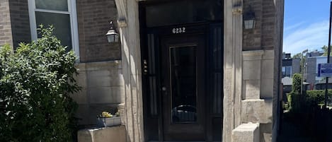 Ein Gebäudeeingang mit einer schwarzen Tür, einer steinernen Fassade und einem schmiedeeisernen Tor mit Verzierungen.