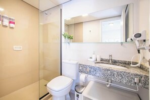 Ein modernes Badezimmer mit einer Duschkabine aus Glas, einer weißen Toilette, einem Waschtisch mit Granitplatte und einem Spiegel über dem Waschbecken.