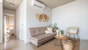 Ein modernes Wohnzimmer mit einem beigen Sofa, einem runden Couchtisch und einem Korbstuhl.
