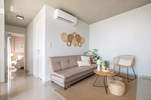 Ein modernes Wohnzimmer mit einem beigen Sofa, einem runden Couchtisch und einem Korbstuhl.