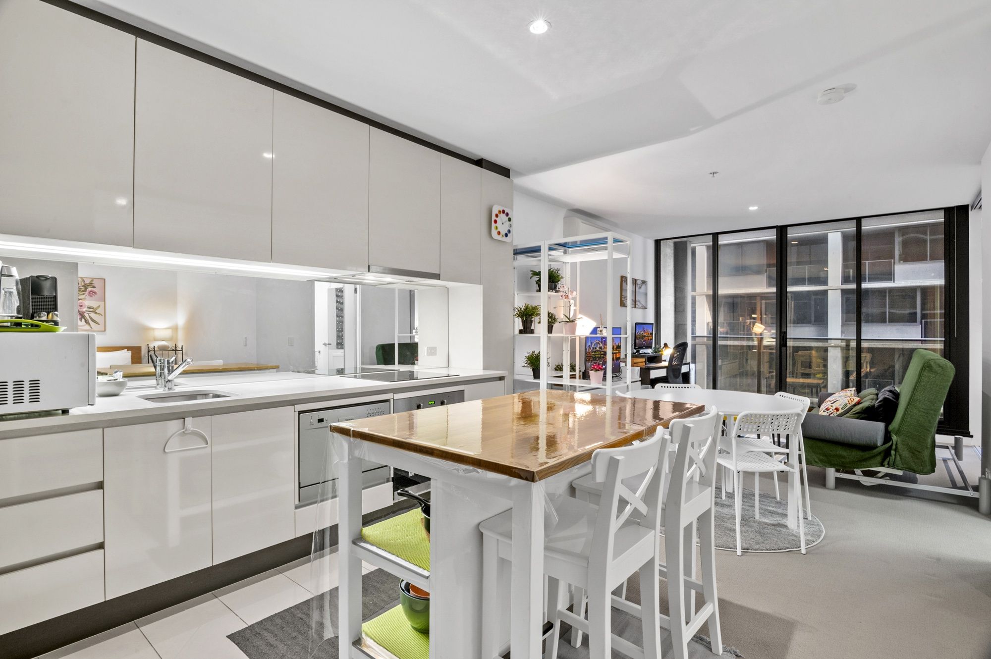 A modern kitchen with white cabinetry, a wooden island, and a dining area with white chairs.