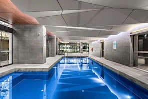 An indoor swimming pool with clear water, surrounded by grey walls and a ceiling with geometric patterns. - City-View 2-Bed Apartment Melbourne CBD (Melbourne)