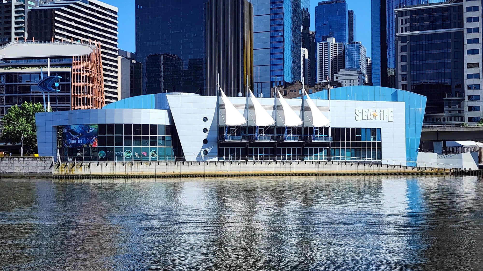 A modern building with a blue and white color scheme, located near a body of water with a reflection.