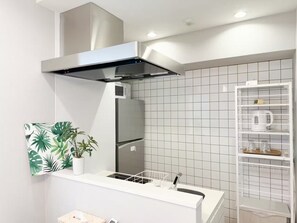 Eine moderne Küche mit einer Edelstahl-Dunstabzugshaube, einer Mikrowelle und einem Kühlschrank. Es gibt ein weißes Regal mit einem Topfpflanzen und eine weiße Schrank mit Gitterablage.
