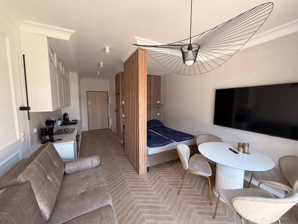 Una habitación de hotel compacta con sofá, una pequeña mesa de comedor, televisión y kitchenette.
