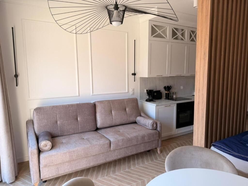 A modern living room with a sofa, a dining table, and a kitchen area in the background.