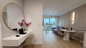 A modern living space with a white desk, a round mirror, a sofa, and a dining area.