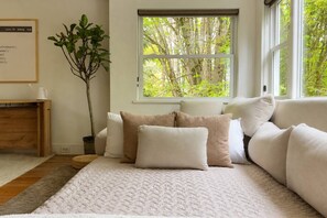 A cozy room with a large window, a plant, and a sofa with cushions. - Beacon Hill Spa Retreat • Sauna • Hot Tub • Cold Plunge • King Bed (Seattle)