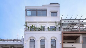 Un edificio de varios pisos con una entrada destacada, un balcón con plantas y un letrero que dice 'AADYA PALACE'.