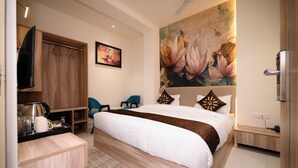 Una habitación de hotel con cama, televisión, un cuadro y un escritorio con hervidor.