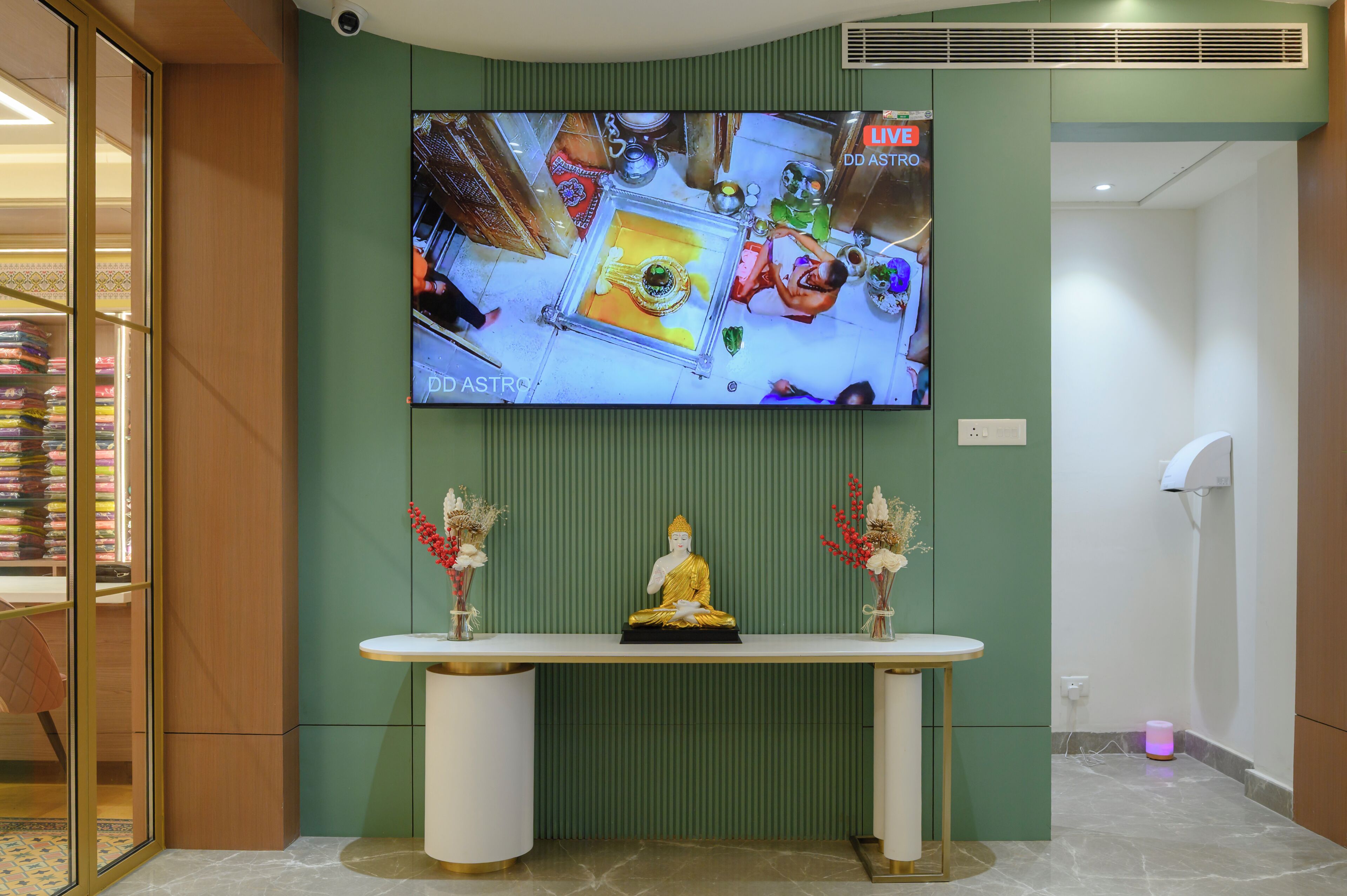 Zona de recepción con televisor montado en la pared, mostrador blanco y una estatua de Buda.