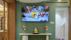 Zona de recepción con televisor montado en la pared, mostrador blanco y una estatua de Buda.