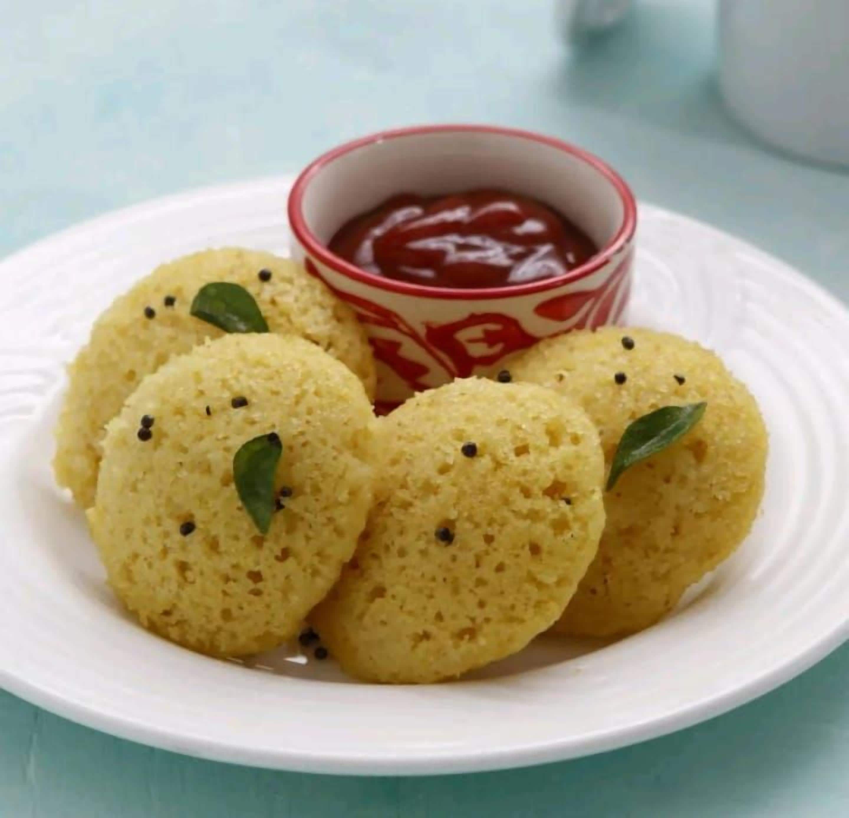 Um prato com quatro aperitivos amarelos, redondos e condimentados, e uma pequena tigela de molho vermelho.
