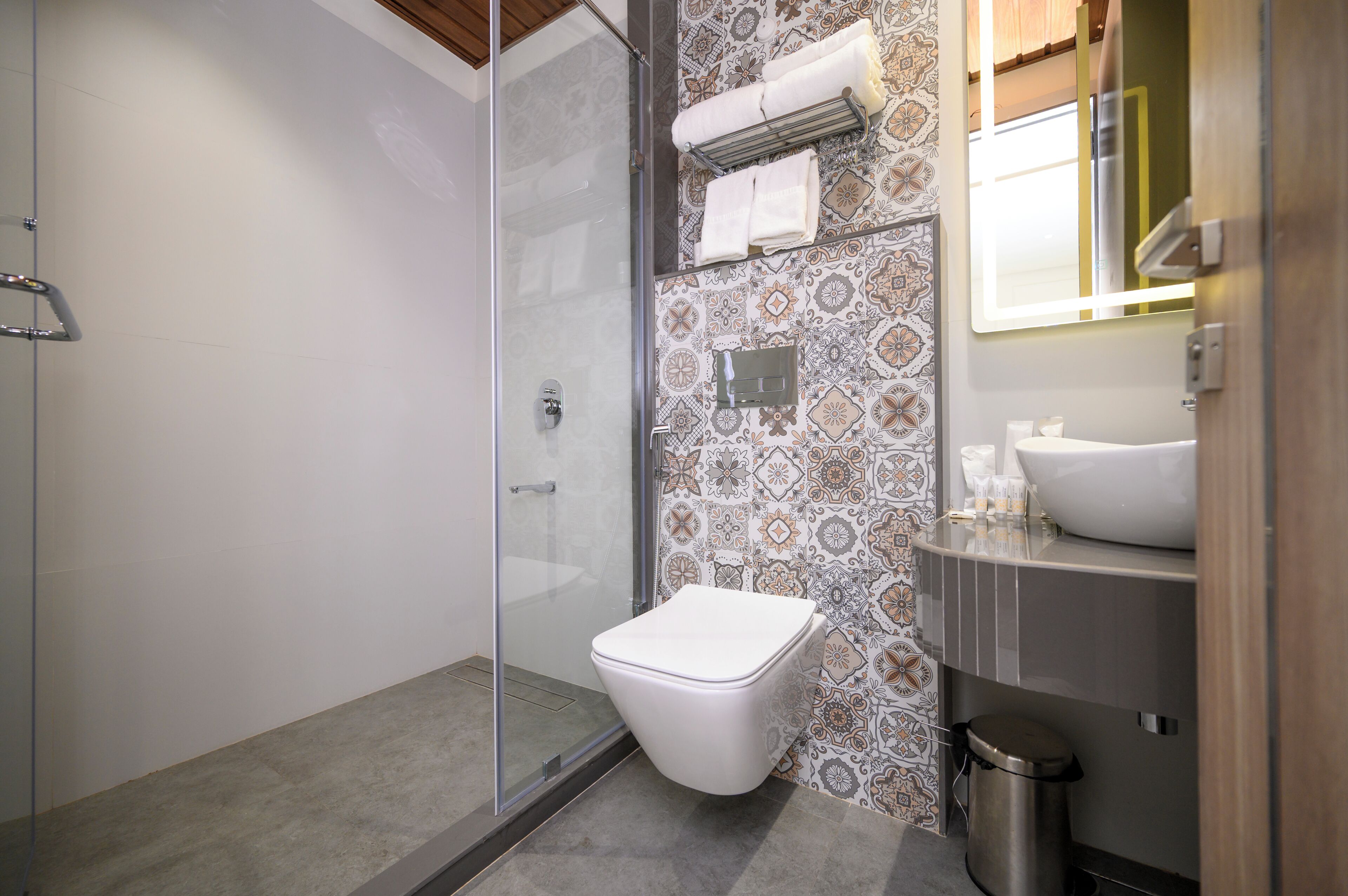 Un baño con cabina de ducha de vidrio, inodoro blanco, azulejos con diseño, un lavabo y un espejo.