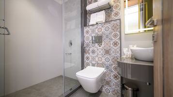 Un baño con cabina de ducha de vidrio, inodoro blanco, azulejos con diseño, un lavabo y un espejo.