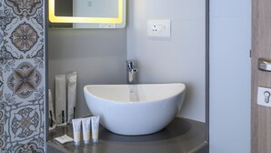 Un baño con lavamanos blanco, un espejo con luz y azulejos estampados.