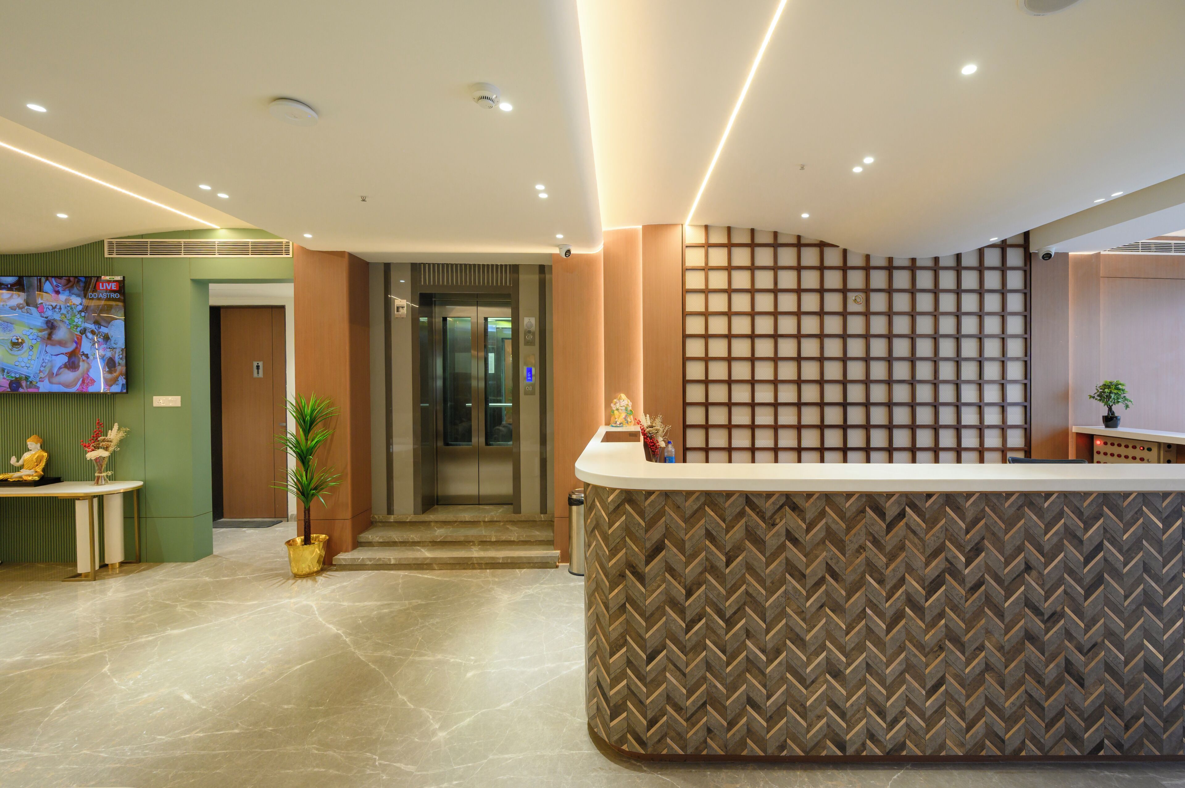 A reception area with a herringbone-patterned counter, a television screen, a reception desk, and a staircase leading to an elevator.