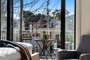 Ein Balkon mit einem kleinen Tisch und Stühlen, Blick auf Gebäude und einem klaren Himmel.