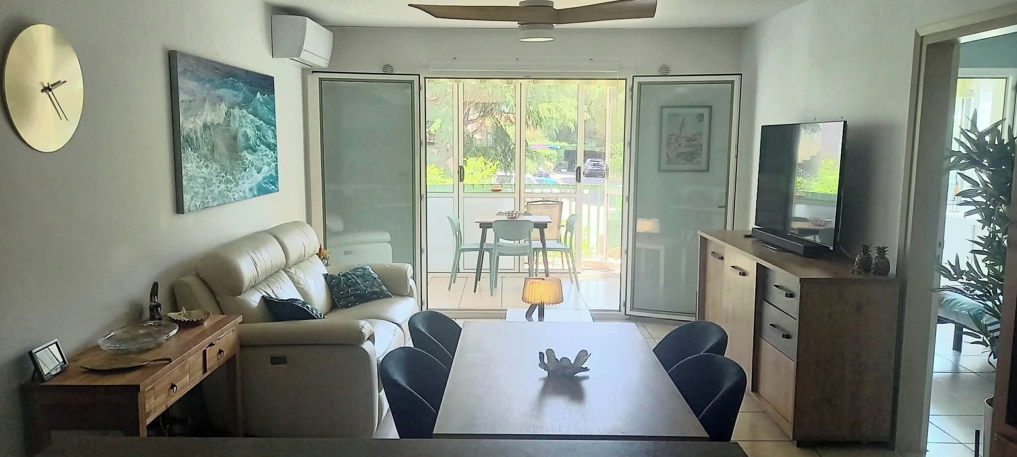 A living room with a sofa, a dining table, a TV, and a large window.