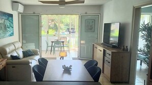 Ein Wohnzimmer mit einer Couch, einem Esstisch, einem Fernseher und einem großen Fenster.