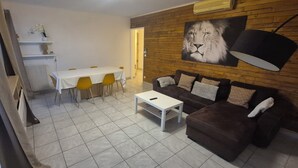 Una sala de estar con un sofá marrón, una mesa de centro blanca, una mesa de comedor con sillas amarillas y un cuadro grande de un león en la pared.