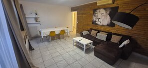 Ein Wohnzimmer mit einem braunen Sofa, einem weißen Couchtisch, einem Esstisch mit gelben Stühlen und einem großen Löwenbild an der Wand.