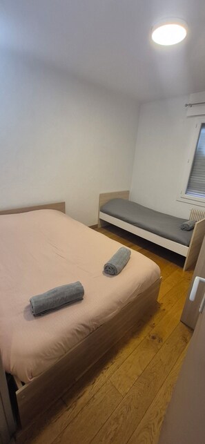 Ein kleiner, gut beleuchteter Raum mit einem Einzelbett, einer Bank und einer Heizung.