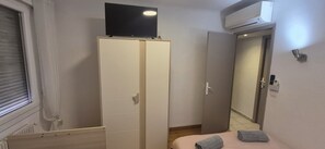 Ein Schlafzimmer mit Kleiderschrank, Bett, Klimaanlage und einem Fenster mit Jalousien.