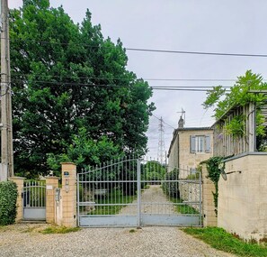 Ein verschlossenes Tor mit einem Kiesweg, der zu einem Gebäude mit Steinmauern und einem Metallgitter führt.