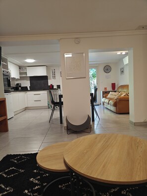 Eine moderne Küche mit weißen Schränken, ein Essbereich mit rundem Tisch und ein Wohnzimmer mit einer Couch.