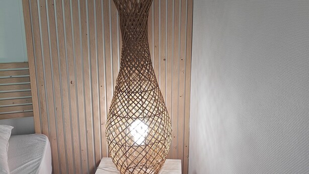 A room with a woven floor lamp on a wooden platform, a bed with white bedding, and a vertical wooden slat wall. - Just 9 minutes from Bordeaux: a getaway along the Garonne River at the 4-star Latresne vacation rental (Latresne)