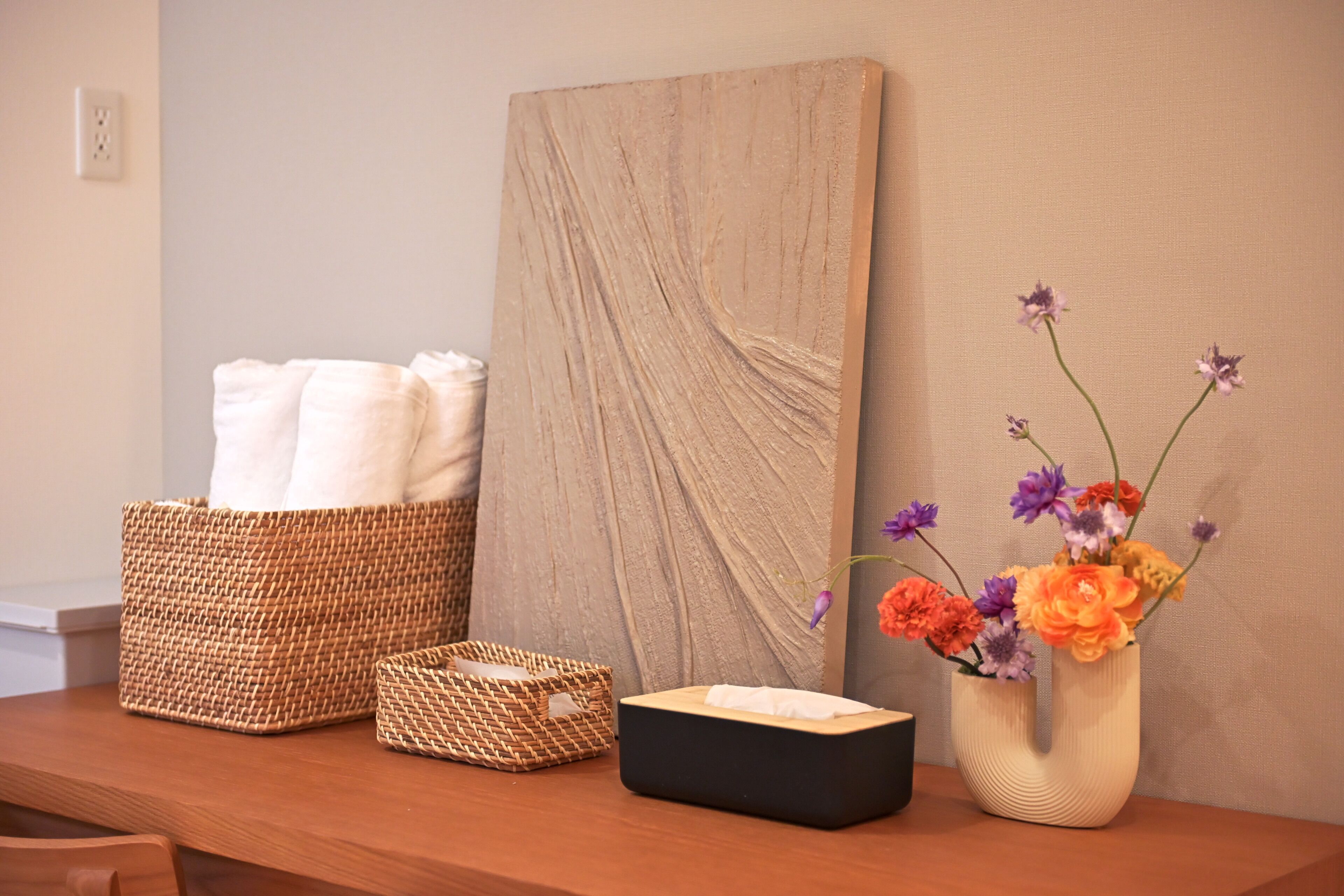 A wooden table with a woven basket, a black box, and a vase with flowers.