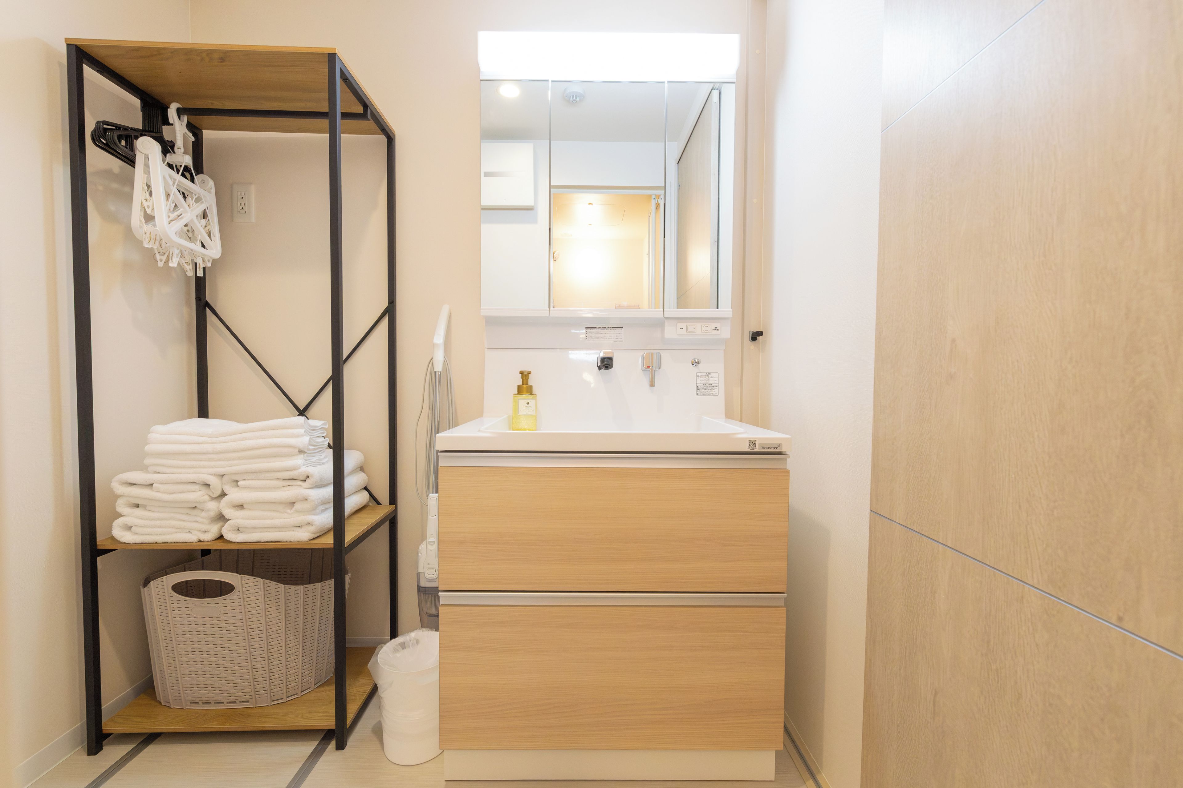 A compact bathroom with a wooden vanity, a mirror, and a shelf with folded towels.