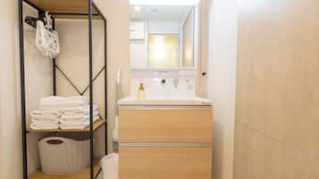 A compact bathroom with a wooden vanity, a mirror, and a shelf with folded towels.