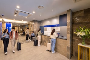A hotel lobby with a reception desk, a digital information board, and a vase with flowers. - NOVI Dotonbori  (CHUO-KU OSAKA)