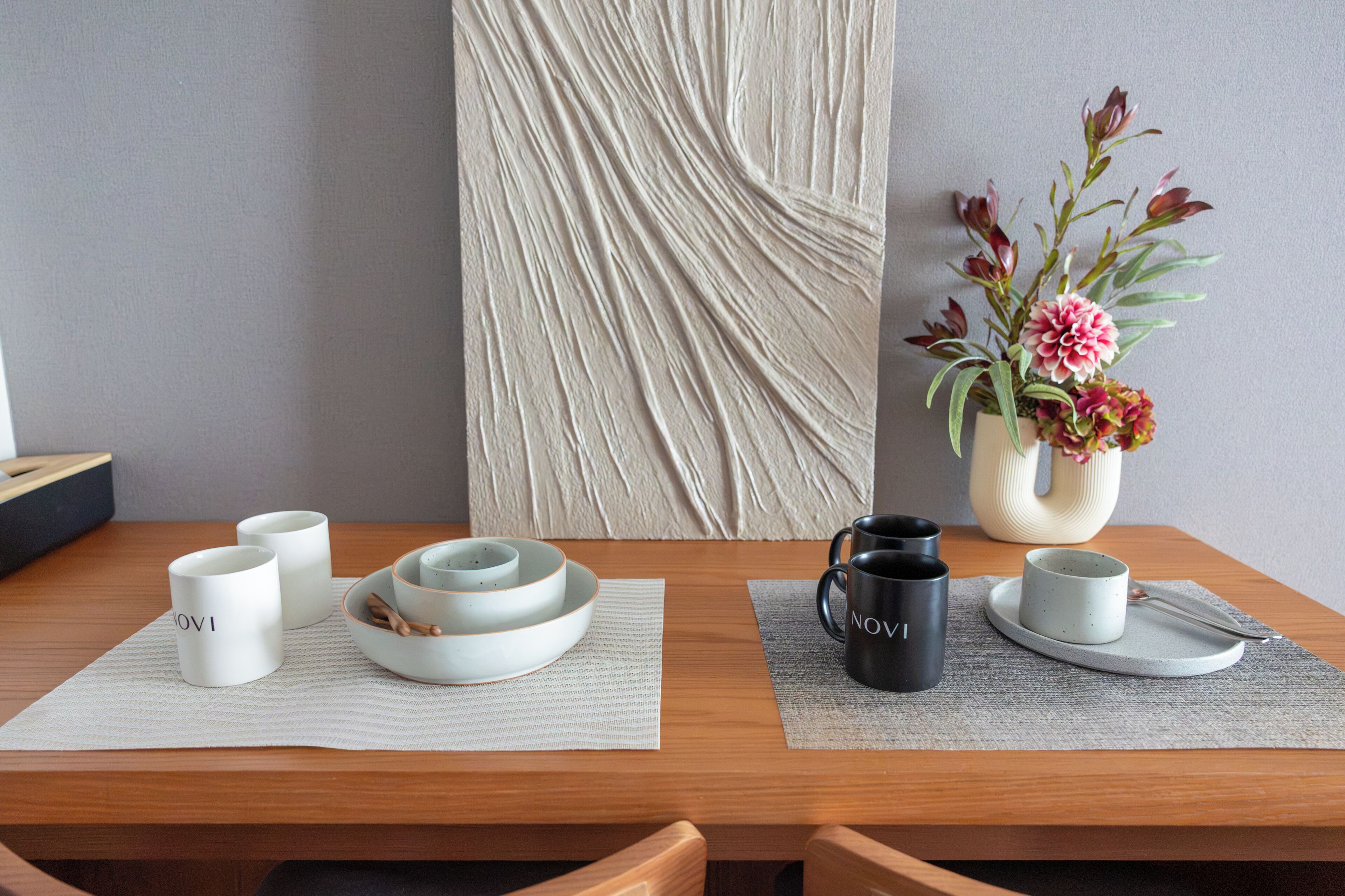 A dining table with a vase of flowers, a placemat, and a set of white and black mugs.
