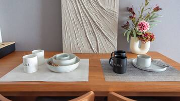 A dining table with a vase of flowers, a placemat, and a set of white and black mugs.