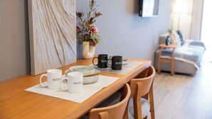 Ett matbord i trä med vita och svarta muggar, en vas med blommor och en tv på väggen.
