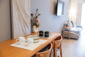 A wooden dining table with white and black mugs, a vase with flowers, and a television on the wall. - NOVI Dotonbori  (CHUO-KU OSAKA)