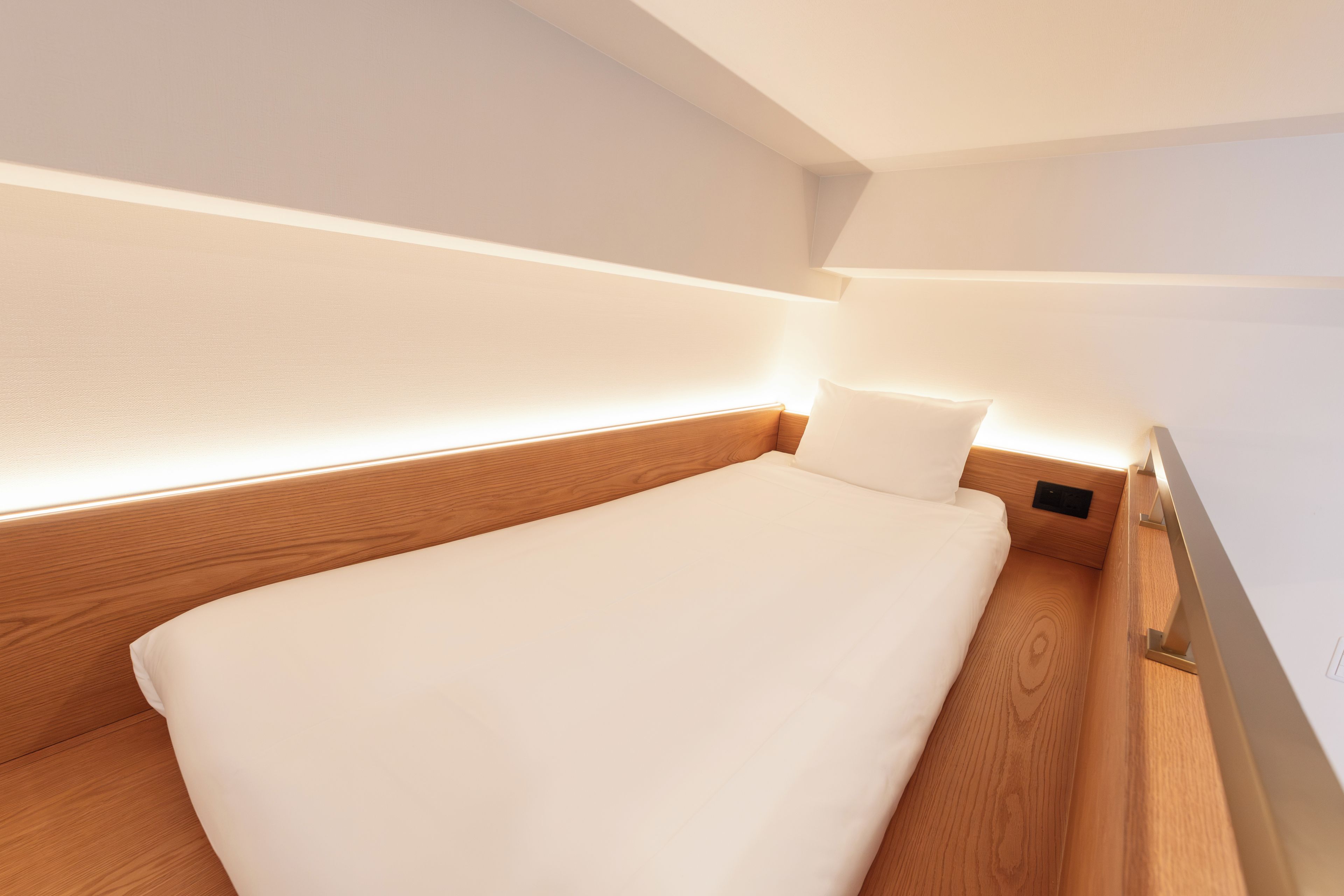 A single bed with a wooden headboard and white bedding in a room with white walls and a sloped ceiling.