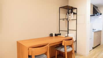 A compact room with a wooden table and two chairs, a small shelf with a bicycle, and a kitchenette in the background.