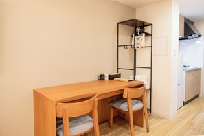 A compact room with a wooden table and two chairs, a small shelf with a bicycle, and a kitchenette in the background. - NOVI Dotonbori  (CHUO-KU OSAKA)