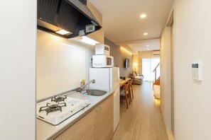 A compact kitchen with a gas stove, microwave, and a small dining area with a table and chairs. - NOVI Dotonbori  (CHUO-KU OSAKA)