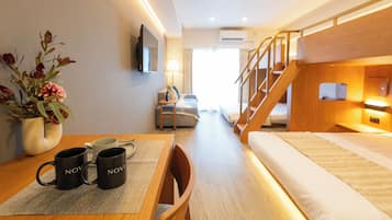 A hotel room with a bunk bed, a desk with a vase of flowers, and a table with two mugs.